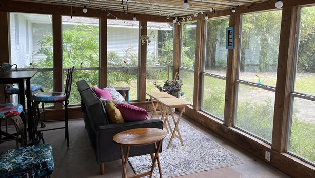Een zonnedek met houten plafond, grote ramen, een bank, een tafel en stoelen.