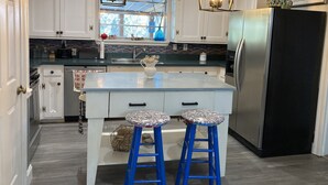 Een moderne keuken met witte kasten, een centraal eiland met krukken, een zwarte koelkast en hanglampen.