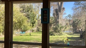 Uitzicht door een raam met houten kader, op een gazon met bomen en een hek.