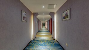A long, narrow hotel corridor with patterned carpet, framed pictures on the walls, and a ceiling with recessed lighting. - Greentree Inn Nanjing Maqun Srt Ningzhi Rd Shell H (Nanjing)