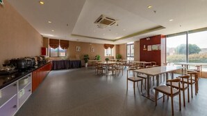 A spacious dining area with multiple tables and chairs, a kitchen area with pots and pans, and large windows offering a view of the outdoors. - Greentree Inn Nanjing Maqun Srt Ningzhi Rd Shell H (Nanjing)