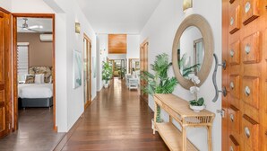 A hallway with wooden flooring, a bed with white bedding, a dining area with white chairs, and a large mirror on the wall. - 54 Ocean Drive Palm Cove (Palm Cove)