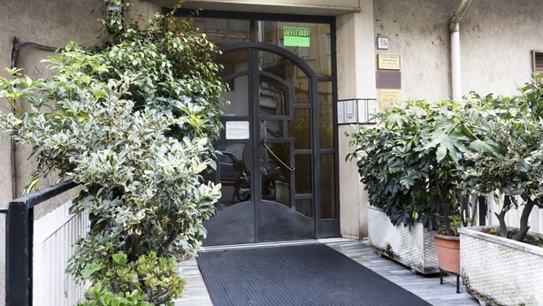 A building entrance with a black door, a green sign, and potted plants.