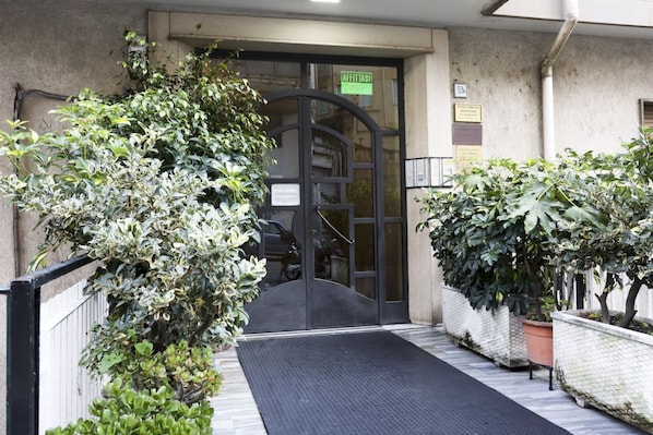 Une entrĂ©e dâimmeuble avec une porte noire, une enseigne verte et des plantes en pot.