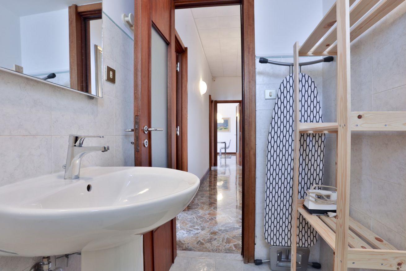 Un bagno con un lavandino bianco, una porta in legno e una zona doccia con tenda da bagno decorata.