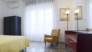 A hotel room with a bed, a chair, a dresser, a mirror, and artwork on the walls.