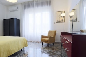 A hotel room with a bed, a chair, a dresser, a mirror, and artwork on the walls.