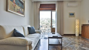 A living room with a sofa, a coffee table, a painting, a view through a window, and a lamp.