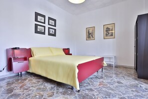 Een slaapkamer met een bed, een nachtkastje, een kledingkast en een wand met ingelijste foto's.
