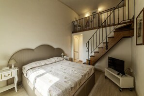 A bedroom with a bed, a nightstand, a TV on a stand, and a staircase.