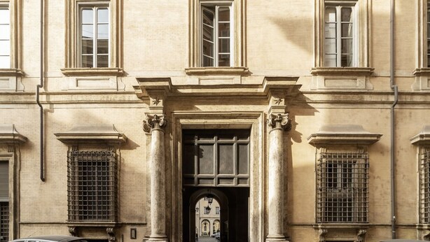 Un bâtiment doté d’une entrée centrale, flanquée de colonnes, et situé le long d’une rue pavée.