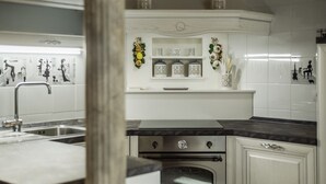 Une cuisine avec des meubles blancs, un évier en acier inoxydable, une cuisinière et des objets décoratifs disposés sur les étagères.