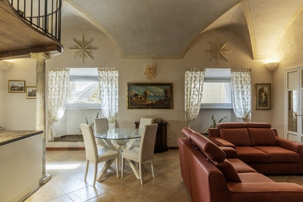 A dining area with a glass table and chairs, a red sofa, and a painting on the wall.