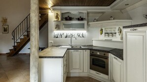 Une cuisine avec des meubles blancs, un four encastré et un escalier en bois.