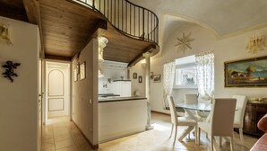 Une cuisine spacieuse dotée d’un îlot central, un coin repas avec des chaises blanches et un escalier menant à l’étage supérieur.