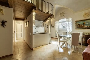 Una cocina amplia con una isla central, un comedor con sillas blancas y una escalera que sube a un nivel superior.