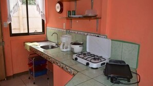 Una cocina compacta con estufa a gas, lavamanos y ventana con cortinas.