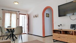 Een moderne woonkamer met een eetgedeelte, een aan de muur bevestigde televisie en een houten kast.