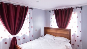 Une chambre à coucher avec un lit en bois, des rideaux rouges et un luminaire blanc au plafond.