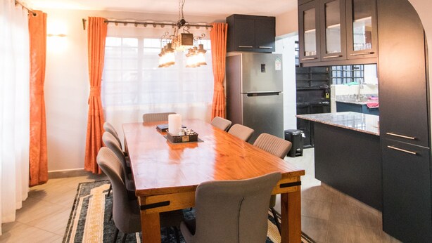 Une cuisine de taille réduite avec des meubles de couleur sombre, une table à manger en bois et un tapis.