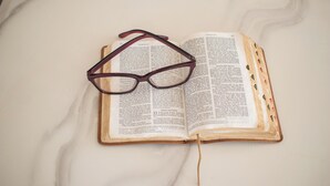 Un livre ouvert, avec des lunettes posées dessus, placé sur une surface blanche.