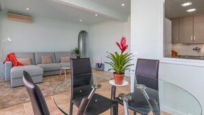 Un salon moderne avec une table à manger en verre, un canapé gris et une plante en pot.