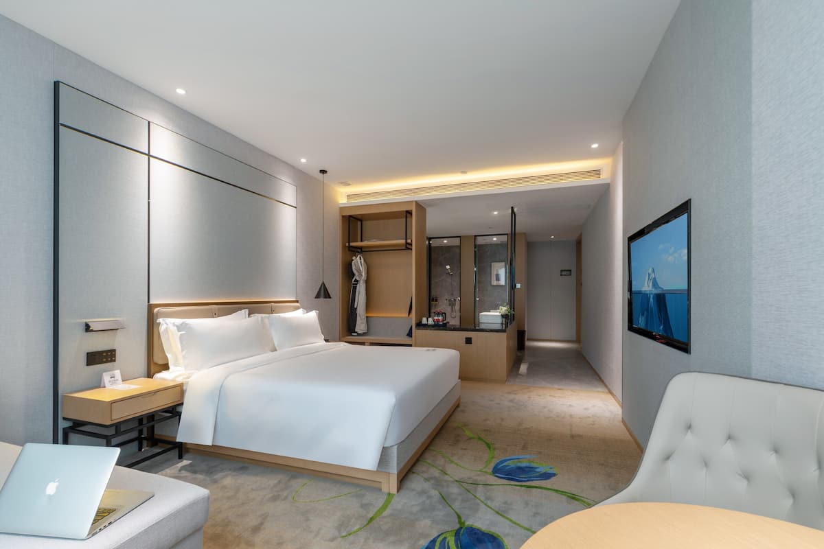 Et moderne hotelværelse med en stor seng, et skrivebord med en bærbar computer, et siddeområde og et fjernsyn på væggen.