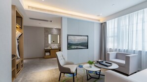 A modern hotel room with a large window, a flat-screen TV, a sofa, a dining table, and a small kitchen area. - Apex Hotel  (Shenzhen)