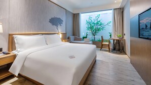 A modern hotel room with a large bed, a desk with a laptop, a chair, and a view of a tree through a window. - Apex Hotel  (Shenzhen)