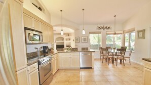 Una cocina amplia con electrodomésticos modernos, un comedor con sillas y ventanas grandes.