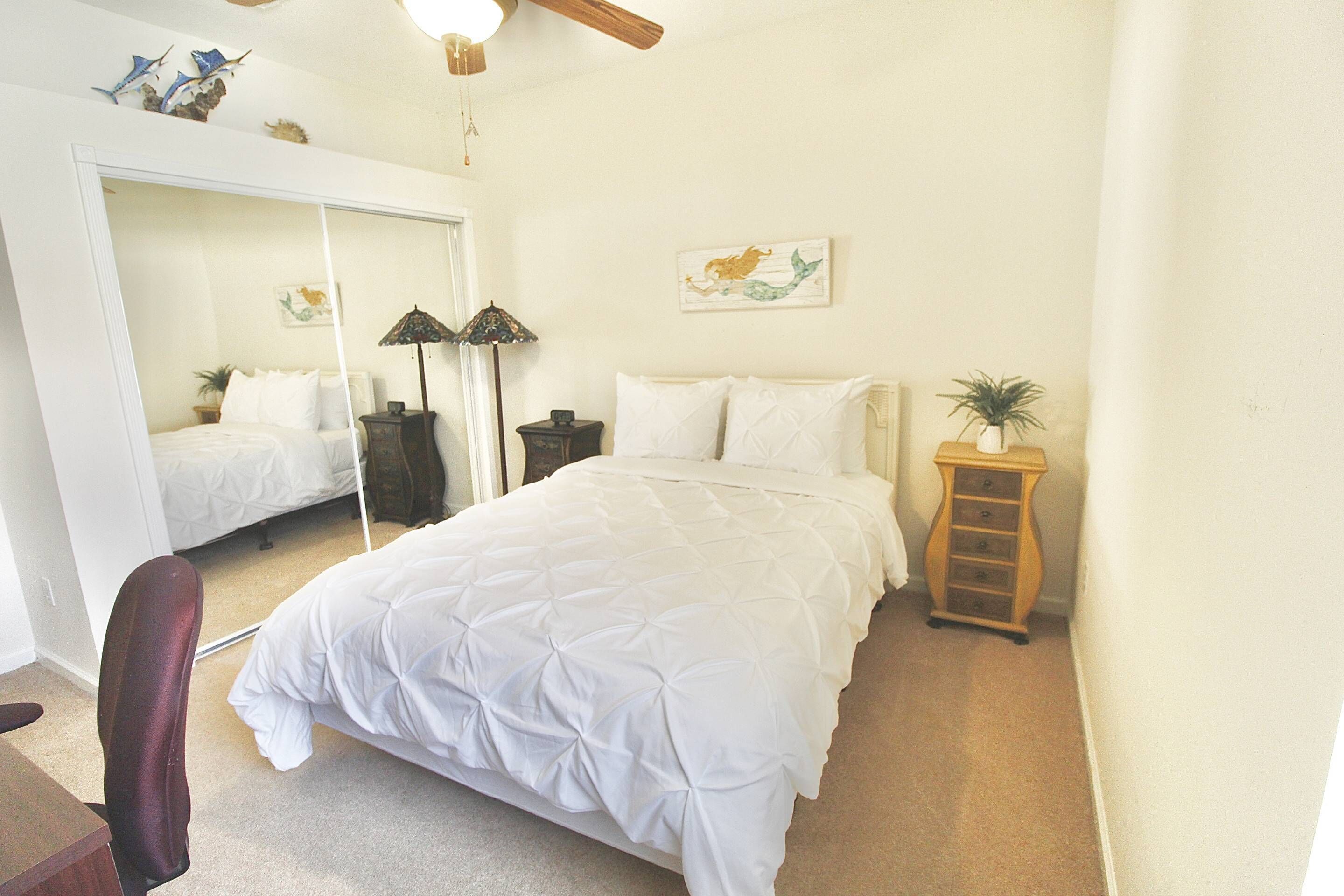 A bedroom with a bed, a chair, a dresser, a mirror, and a ceiling fan.