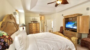 Un dormitorio con una cama grande, cabecera de madera, televisor, cómoda y ventilador de techo.