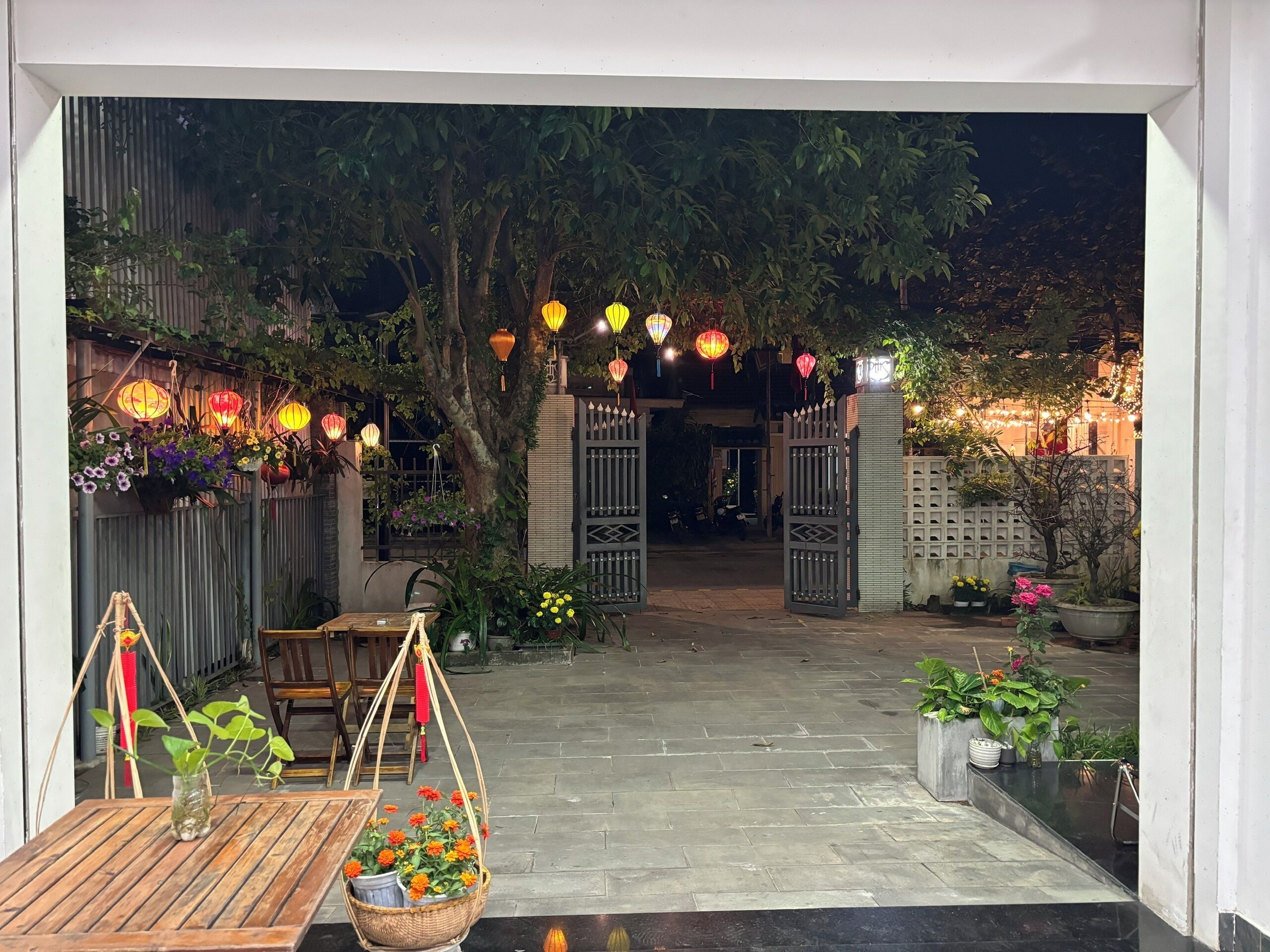 Une cour avec une table en bois, des lanternes suspendues et des plantes en pot.