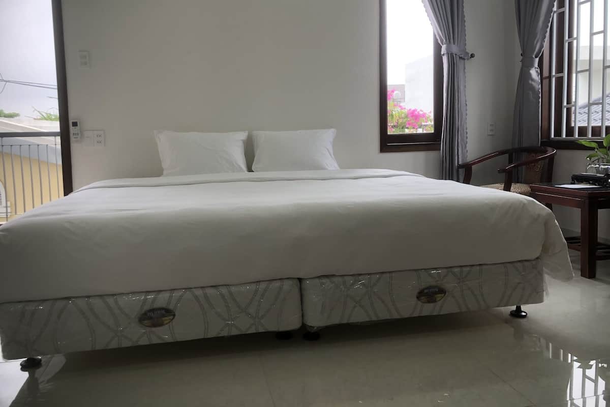 A neatly made bed with a white comforter and pillows, a wooden nightstand with a lamp, and a window with curtains.