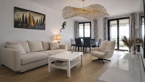 Un salon moderne comprenant un canapé, un fauteuil, une table basse et un tableau représentant des voiliers.