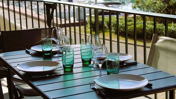 Une table dressée pour le dîner, avec en arrière-plan une vue sur des bateaux.
