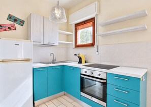 A compact kitchen with white cabinets, a black stove, and a window with a curtain. - Vania, in Marina di Campo, is located in a residential area, convenient to the beach and services, w (Campo nell'Elba)