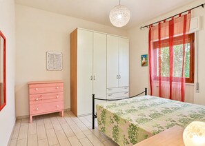 A bedroom with a bed, a wardrobe, a dresser, a window with curtains, and a hanging light fixture.