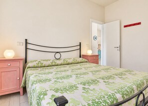 Une chambre à coucher comprenant un lit, des tables de chevet, une commode, une lampe, une porte et un interrupteur fixé au mur.