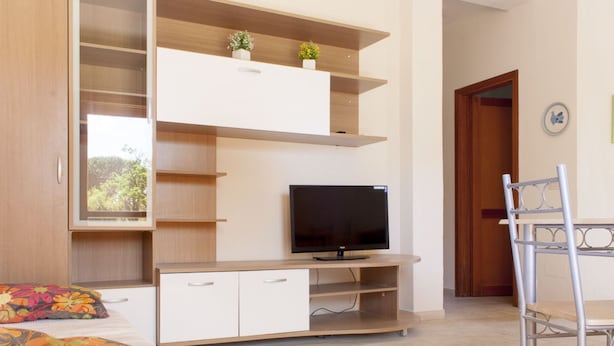 A modern bedroom with a bed, a TV on a wooden stand, a desk with a chair, and built-in shelving with plants. - Vania, in Marina di Campo, is located in a residential area, convenient to the beach and services, w (Campo nell'Elba)