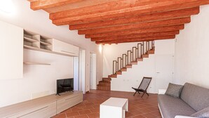 Ein modernes Wohnzimmer mit Holzboden, einer Treppe, einem grauen Sofa, einem Fernseher auf einer Holzkommode und einem Fliesenboden.