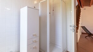 Ein Badezimmer mit weiß gefliesten Wänden, einem weißen Schrank mit Schubladen und einer Duschkabine aus Glas.