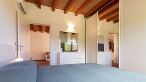 Ein Schlafzimmer mit einem großen Bett, einem Fernseher auf einer Kommode und einer Holzbalkendecke.