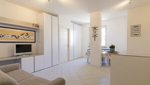Un salón moderno y bien iluminado con un sofá, un televisor de pantalla plana y una mesa de comedor con sillas.