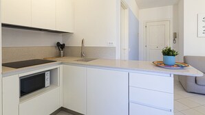 Una cocina compacta con armarios blancos, un microondas integrado, un lavamanos de acero inoxidable y una pequeña planta en maceta sobre la encimera.