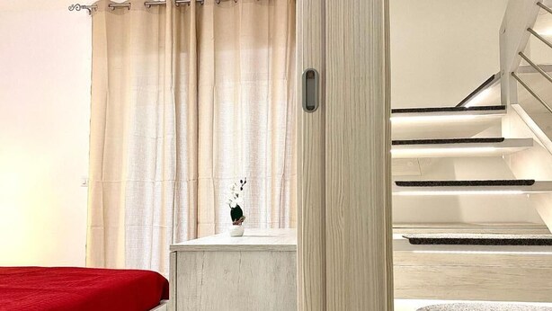 A bedroom with a bed, a nightstand, a potted plant, and a staircase. - Monopoly Sky House (Monopoli)