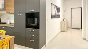 A modern kitchen with grey cabinets, a built-in oven, and a dining area with yellow chairs. - Monopoly Sky House (Monopoli)