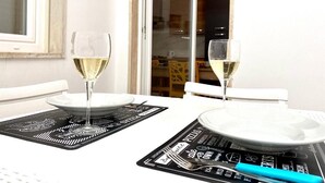 A dining table set with two wine glasses, plates, and a fork on a black placemat with white text. - Monopoly Sky House (Monopoli)
