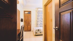 A hallway with a bed, a chair, and a wooden door. - PIA Hotel Medan (Medan)