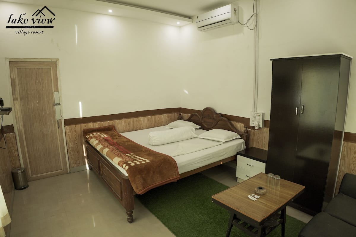 A hotel room with a bed, a wardrobe, a small table, and a trash bin.